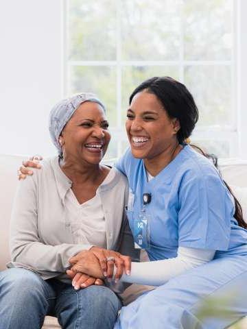 在她访问期间, 中年成年家庭保健护士与老年成年癌症妇女相拥而笑.